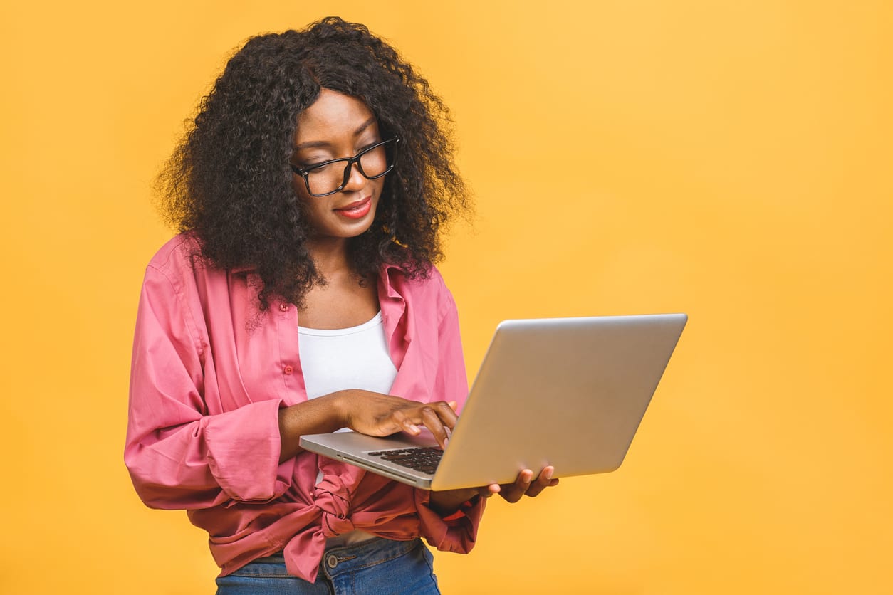 Young_african_american_black_positive_cool_lady_with_curly_hair_using_laptop_and_smiling_isolated_over_yellow_background