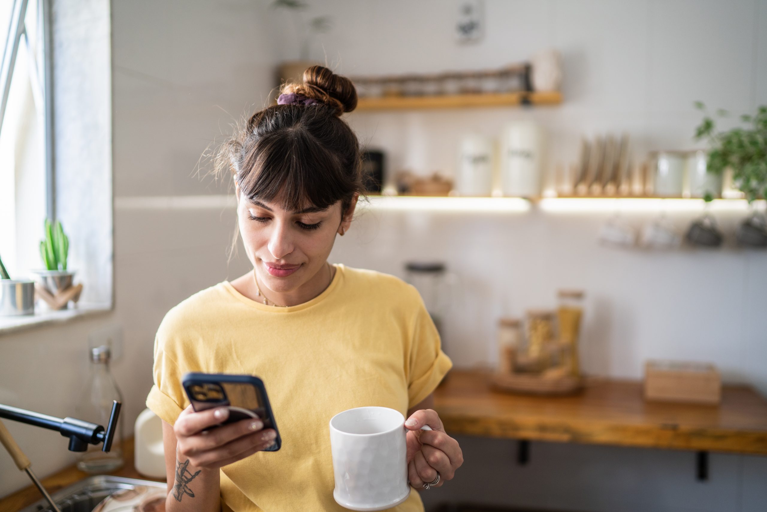 Young-woman-using-the-mobile-phone-while-drinking-coffee-or-tea-at-home